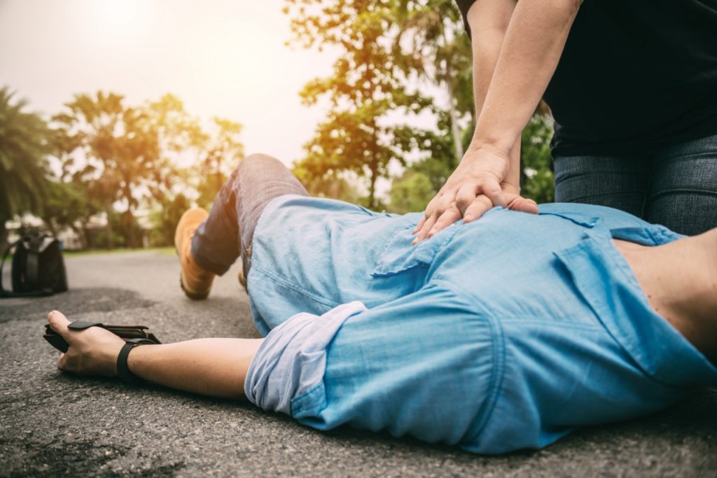 man in cardiac arrest laying on the ground receiving emergency CPR from a bystander